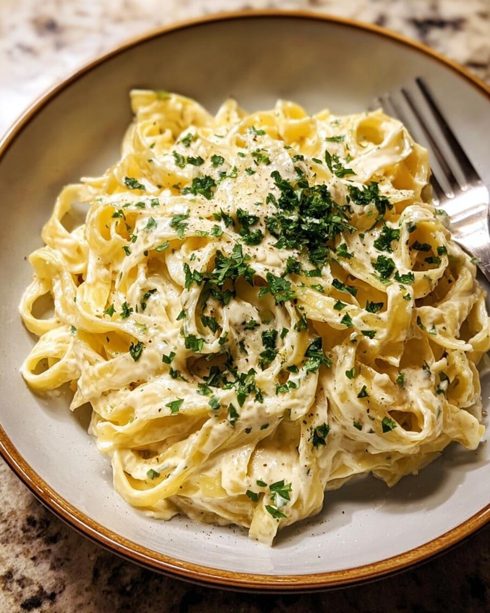A close-up of fettuccine pasta coated in a rich, Creamy Alfredo Sauce, garnished with fresh parsley.