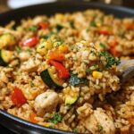 A close-up of a creamy chicken and rice skillet with colorful vegetables like zucchini, bell peppers, and corn, garnished with parsley.