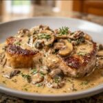 A close-up of delicious Creamy Mushroom Pork Chops in a pan, smothered in a rich mushroom sauce and garnished with herbs.