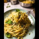 A fork twirls a portion of Garlic Butter Pasta with Parmesan and Herbs, garnished with fresh basil leaves.