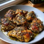 A close-up of perfectly cooked Greek Style Chicken with Garlic and Oregano in a pan, glistening with juices and herbs.