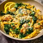 A close-up of a bowl of Lemon Chicken Pasta with Spinach and Parmesan, garnished with lemon slices.