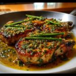 Three pan-seared Lemon Herb Pork Chops with Bright Zest, glistening in a savory sauce and garnished with fresh herbs.
