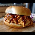 A close-up of a BBQ Chicken Sandwich Filling that shreds perfectly, piled high on a bun with BBQ sauce.