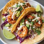 Two delicious Shrimp Tacos with Creamy Lime Sauce, filled with shrimp, avocado, red cabbage, and cilantro.