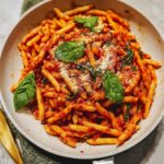 A close-up of Spicy Arrabbiata Pasta with Bold Heat, coated in a rich tomato sauce and garnished with fresh basil and Parmesan cheese.