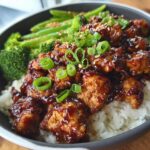 A close-up of a Sticky Teriyaki Chicken Bowl with fresh crunch, featuring glazed chicken pieces over rice with broccoli and green onions.