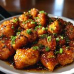 Close-up of delicious Sweet and Spicy Honey Garlic Chicken Bites, glazed and topped with sesame seeds and green onions.