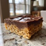 A close-up of a decadent Chocolate Peanut Butter Bar, showing layers of peanut butter, caramel, and chocolate.