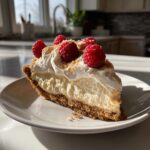 A slice of No Bake Coconut Cream Pie topped with whipped cream, raspberries, and toasted coconut flakes.