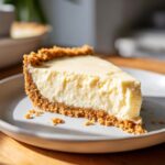 A close-up of a slice of no bake lemon cheesecake with a graham cracker crust.